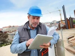 Site manager in a hard hat reviewing a tablet on a construction site